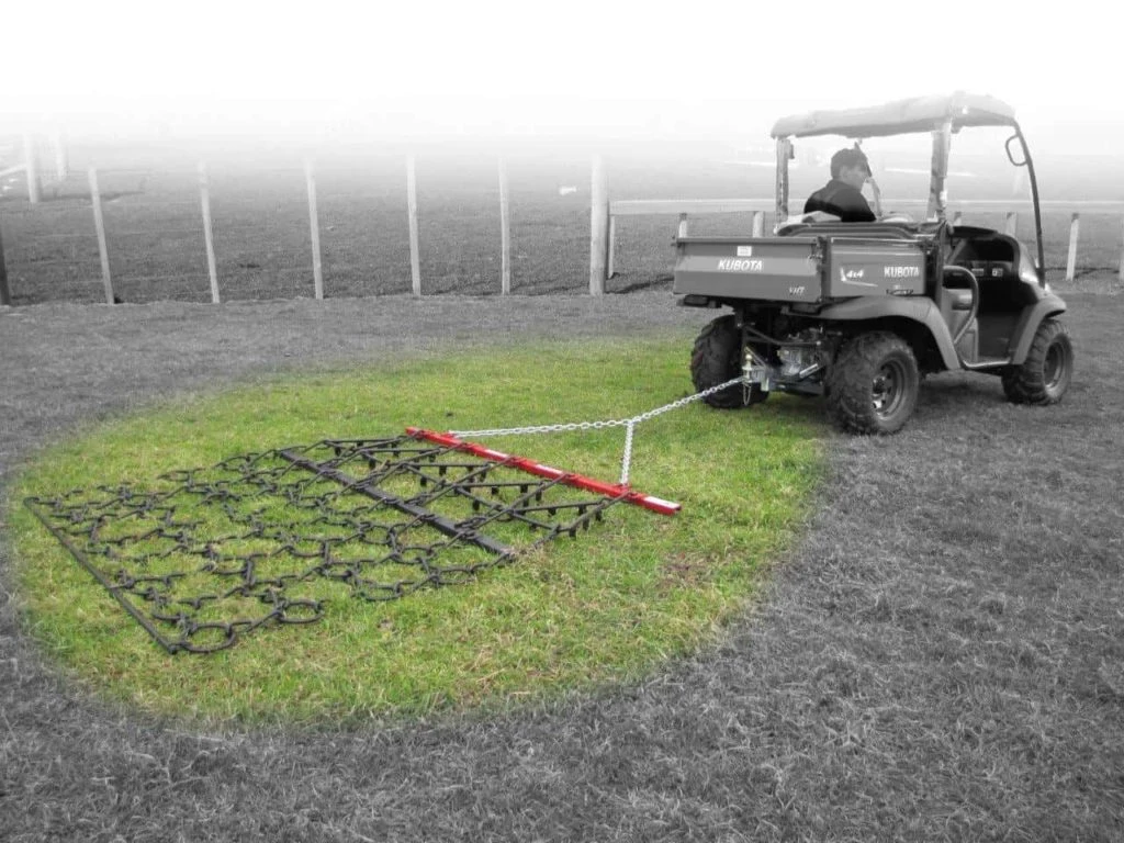 Chain harrow being towed across a paddock by a utility vehicle